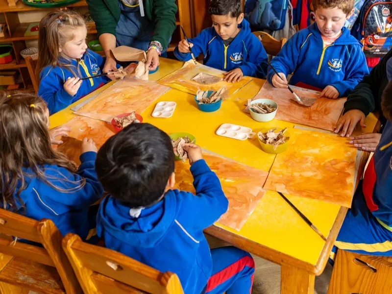 Niños pintando en grupo con corteza y témpera en el Jardín Infantil Arco Iris en Concón