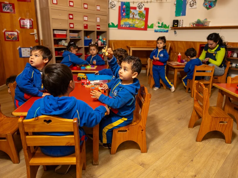 Niños y niñas en una sala con mesas rojas del Jardín Infantil Arco Iris en Concón